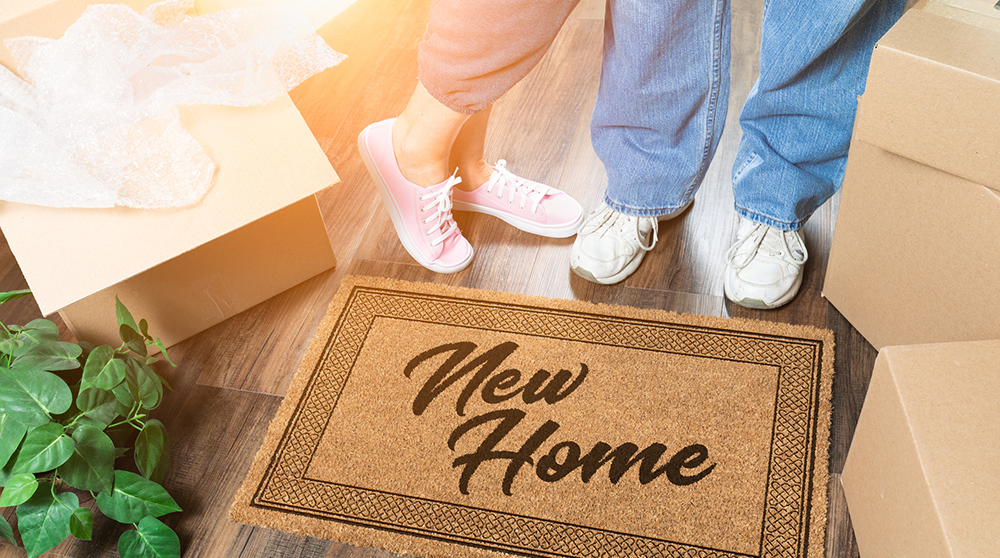 Couple standing next to a new house welcome mat surrounded by moving boxes after a home inspection